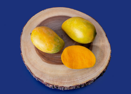 Three mangoes on a wooden slice against a blue background
