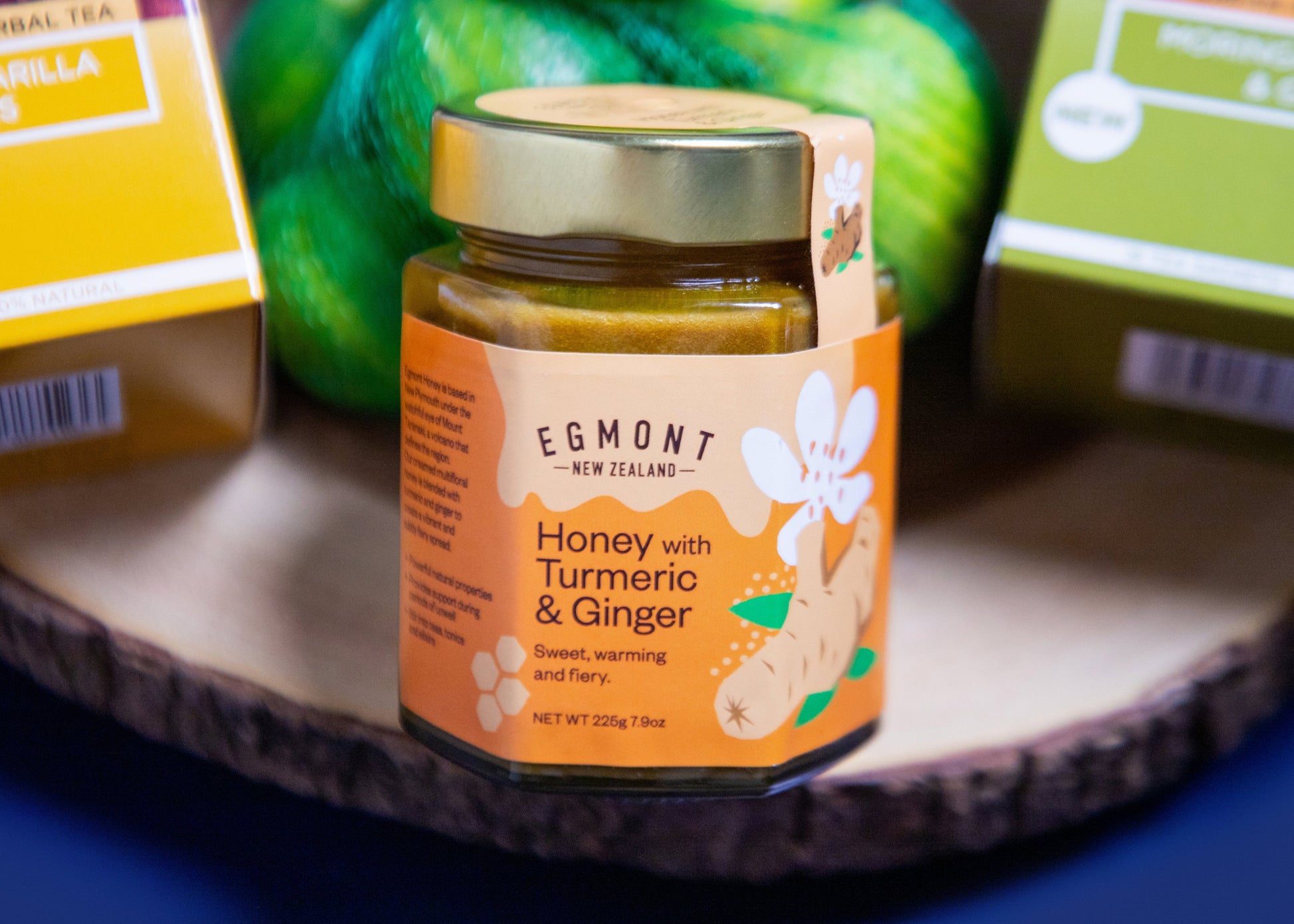 Jar of Egmont honey with turmeric and ginger on a wooden surface with other products in the background.