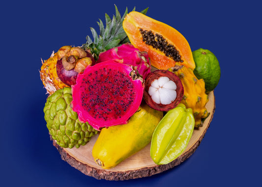 Assorted tropical fruits on a wooden plate against a blue background